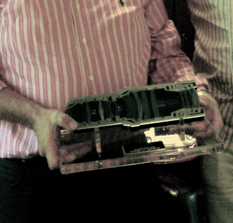 Two people hold a large precision lens formerly used in ASML chipmaking equipment